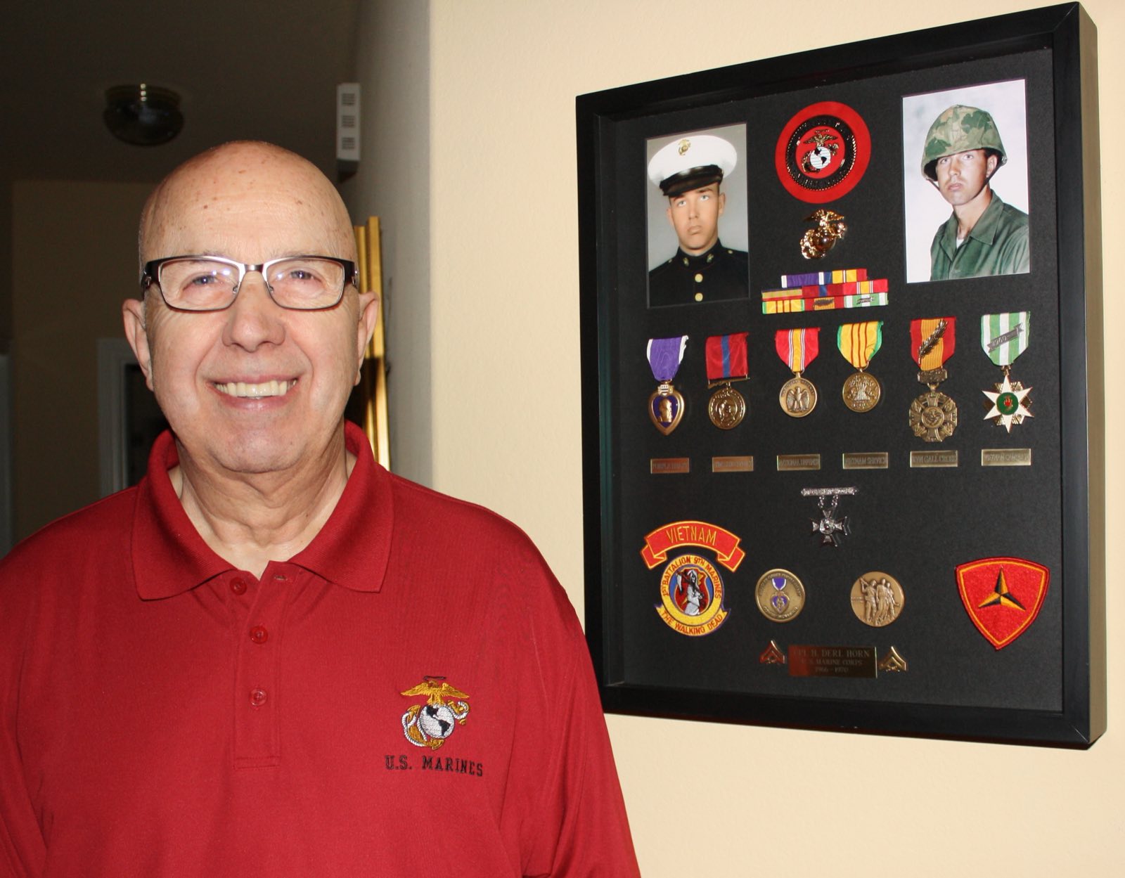 Derl Horn today, standing beside a framed shadow box displaying his medals and service ribbons